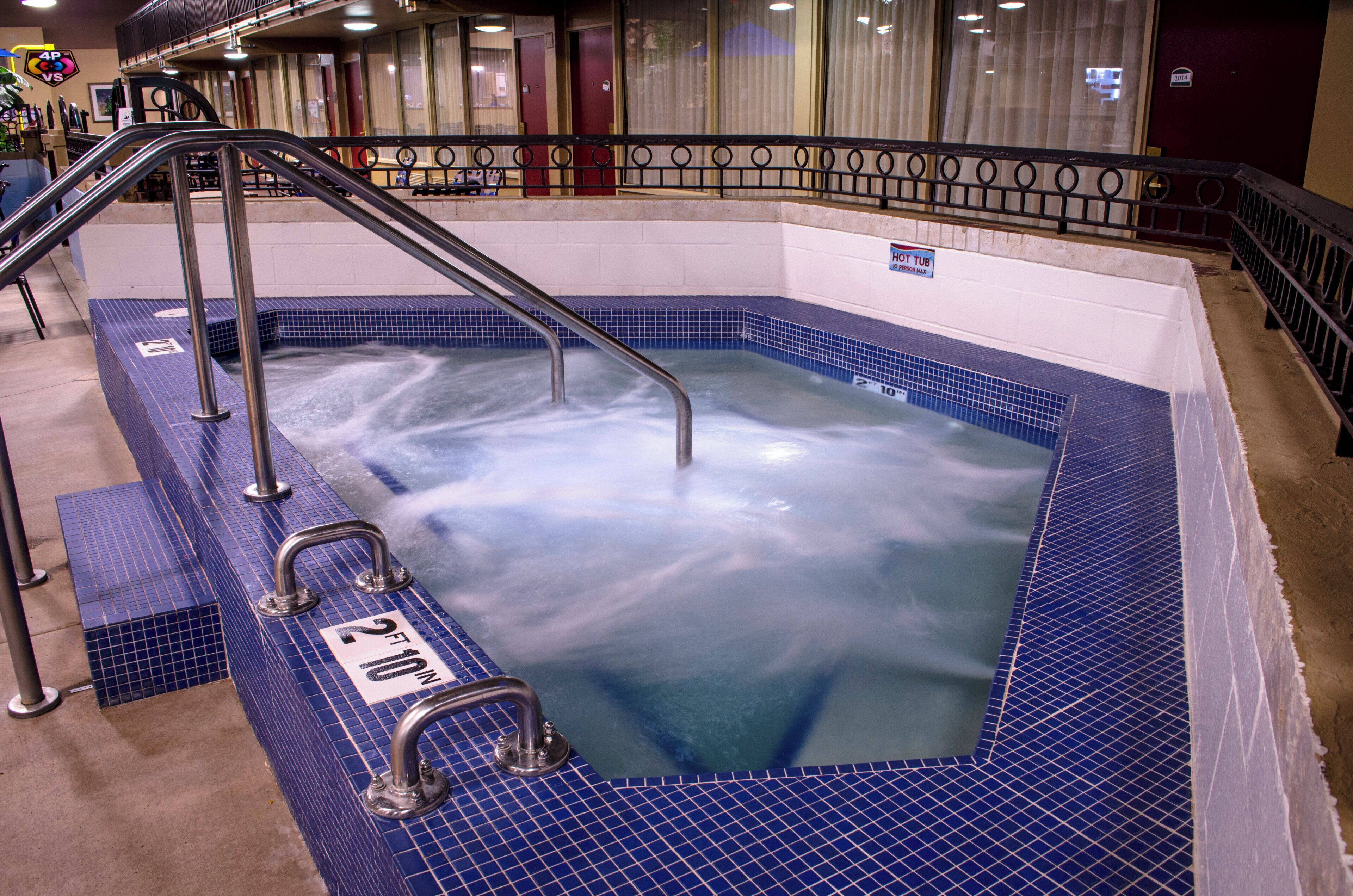 A hot tub with a metal ladder and railings, surrounded by a tiled floor.
