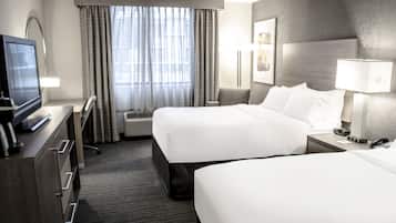 A hotel room with two beds, a desk with a TV, a lamp, and a framed picture on the wall.