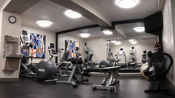 Ett gym med olika typer av träningsutrustning, en vattenautomat och en klocka på väggen.