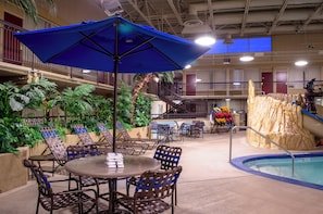 An indoor pool area with lounge chairs and umbrellas, surrounded by greenery and a statue. - Holiday Inn Fargo by IHG (Fargo)