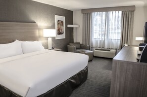 Ein Hotelzimmer mit einem großen Bett, einem Schreibtisch, einem Stuhl, einer Couch, einer Lampe und einem Fenster mit Vorhängen.