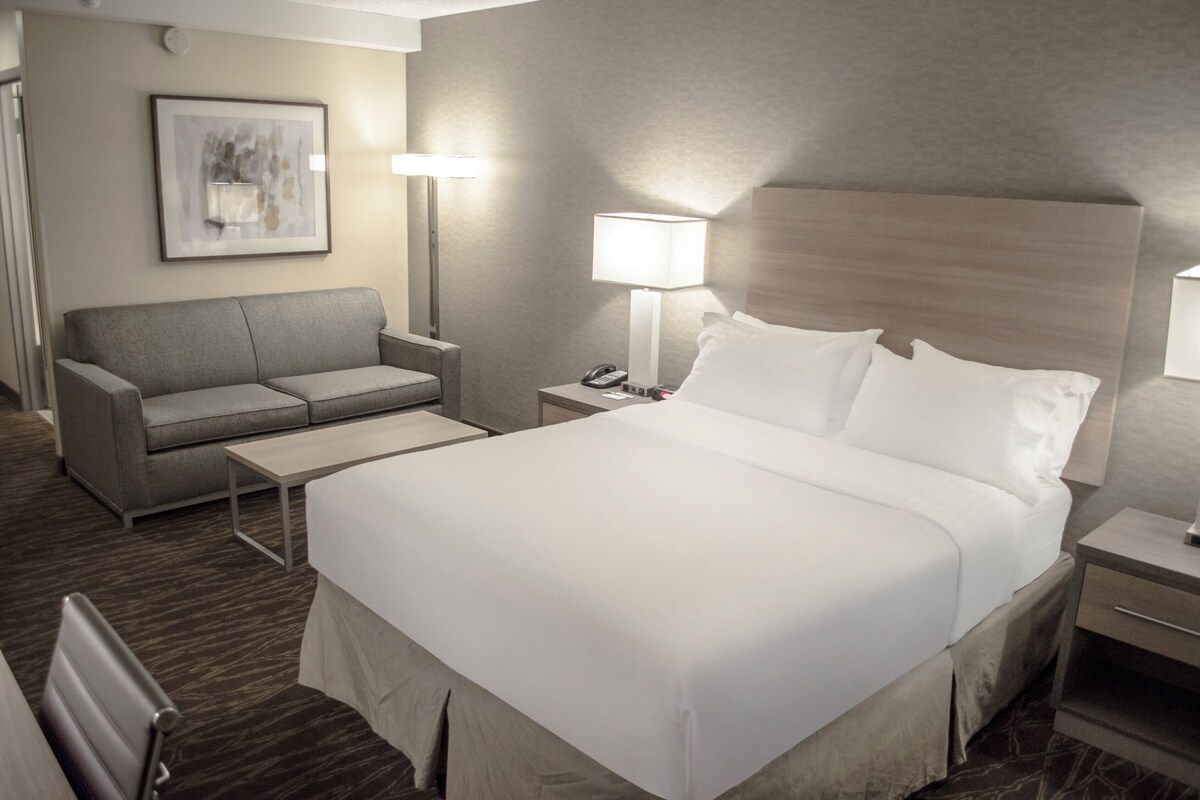 Ein Hotelzimmer mit Bett, Sofa, Schreibtisch und Nachttisch mit Lampe.
