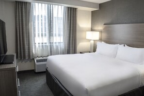A hotel room with a large bed, a desk with a laptop, a lamp, and a window with curtains.