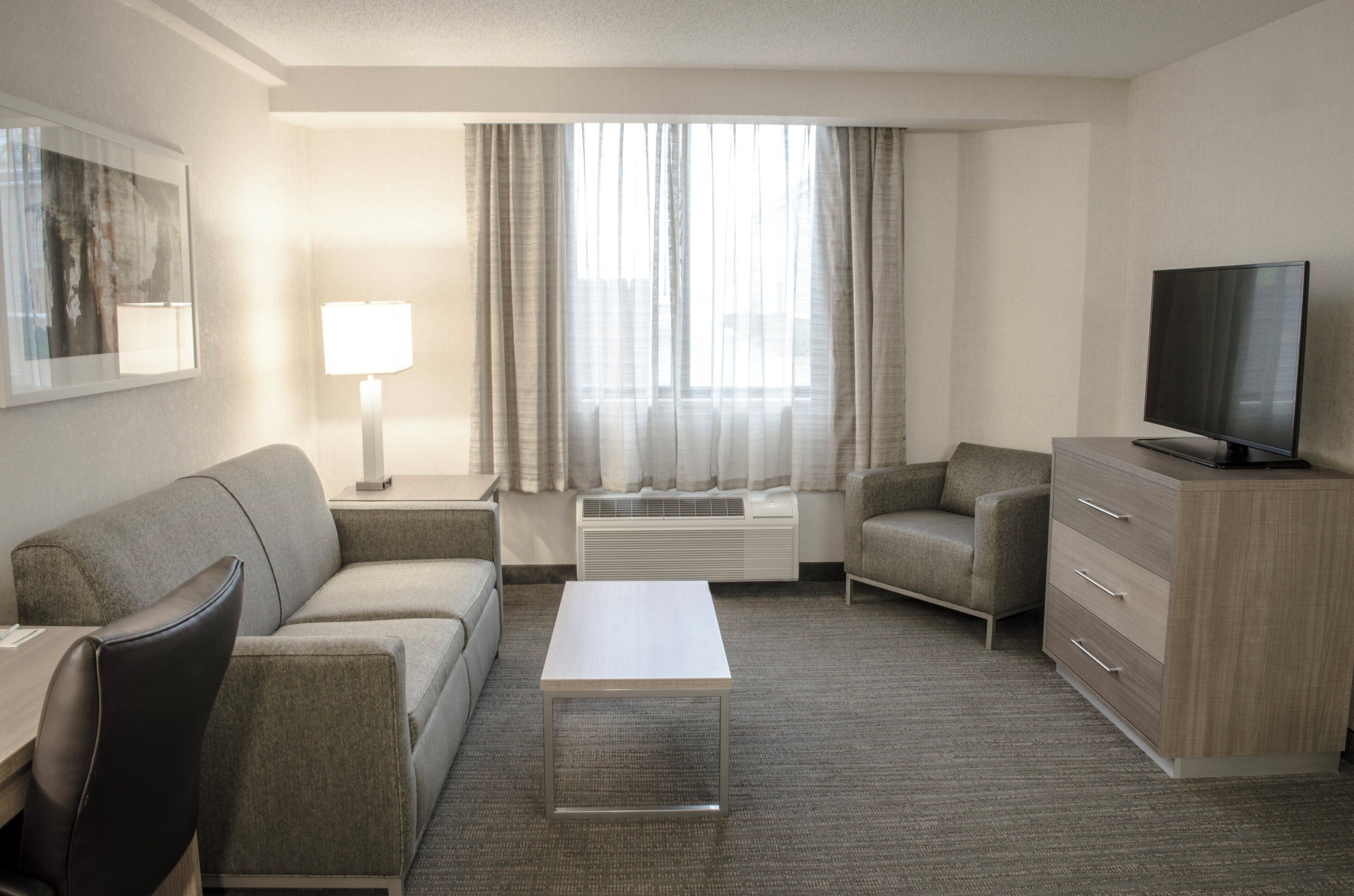 A hotel room with a sofa, a chair, a coffee table, a TV, and a dresser.