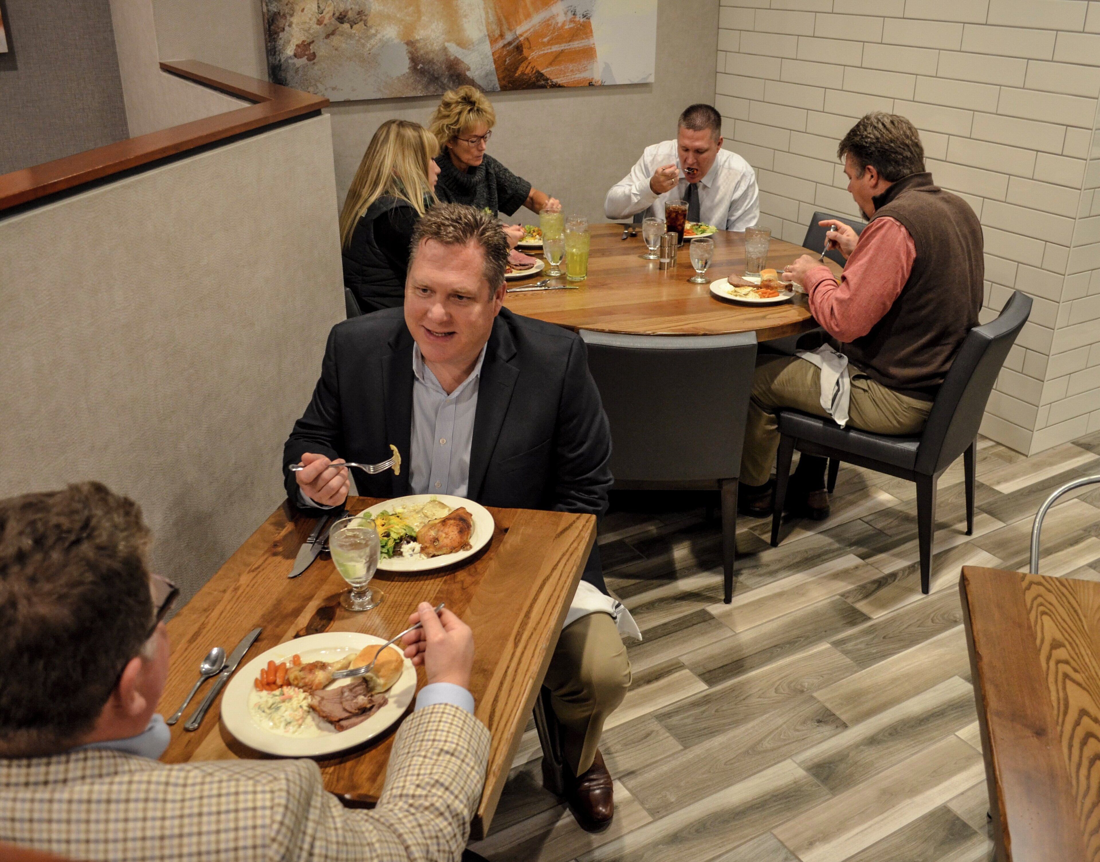 A group of people dining at a round table in a room with a herringbone floor pattern.