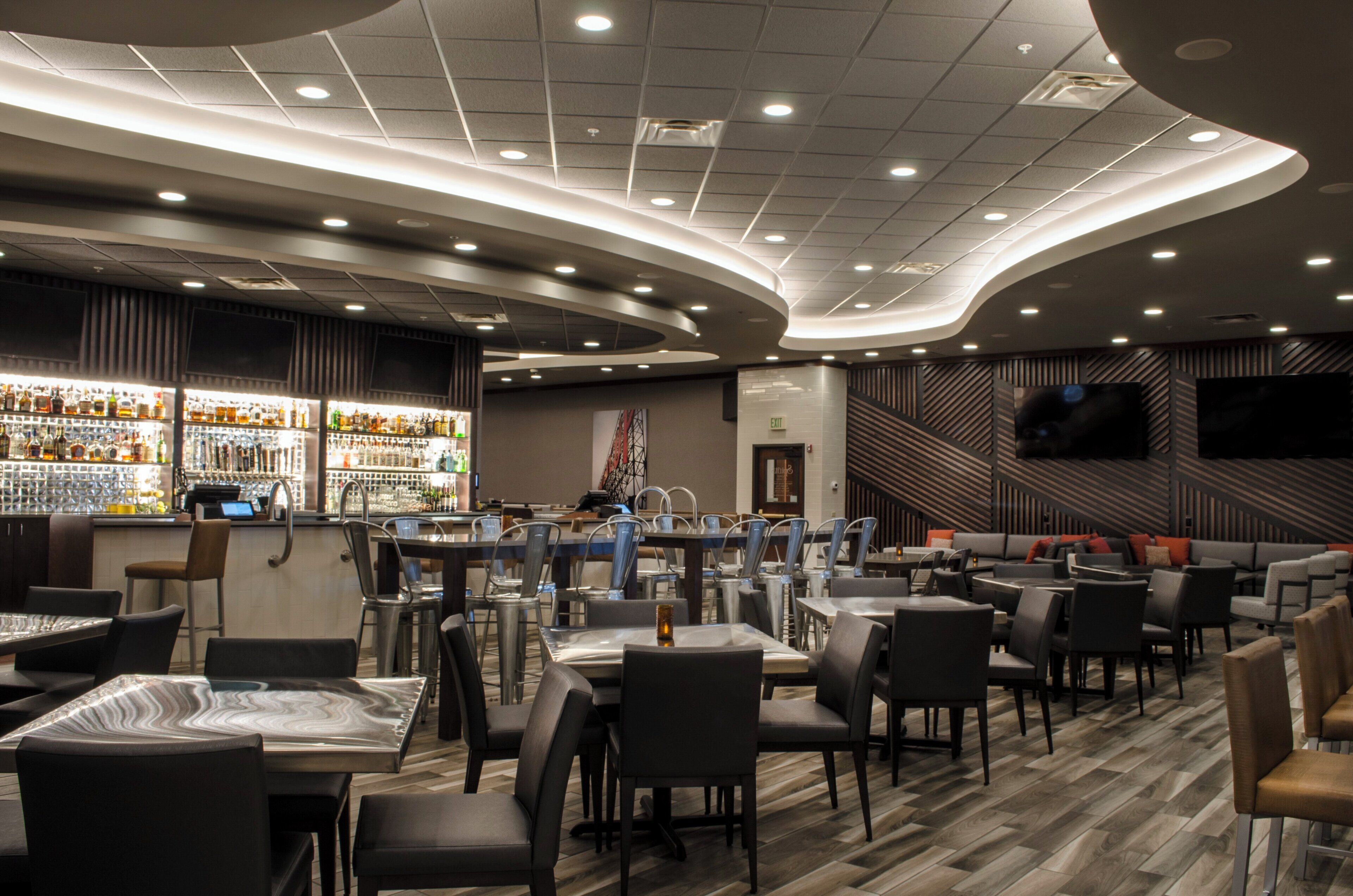 A modern restaurant interior with a bar area, seating arrangements, and a flat-screen TV mounted on the wall.