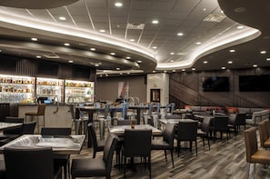 A modern restaurant interior with a bar area, seating arrangements, and a flat-screen TV mounted on the wall.