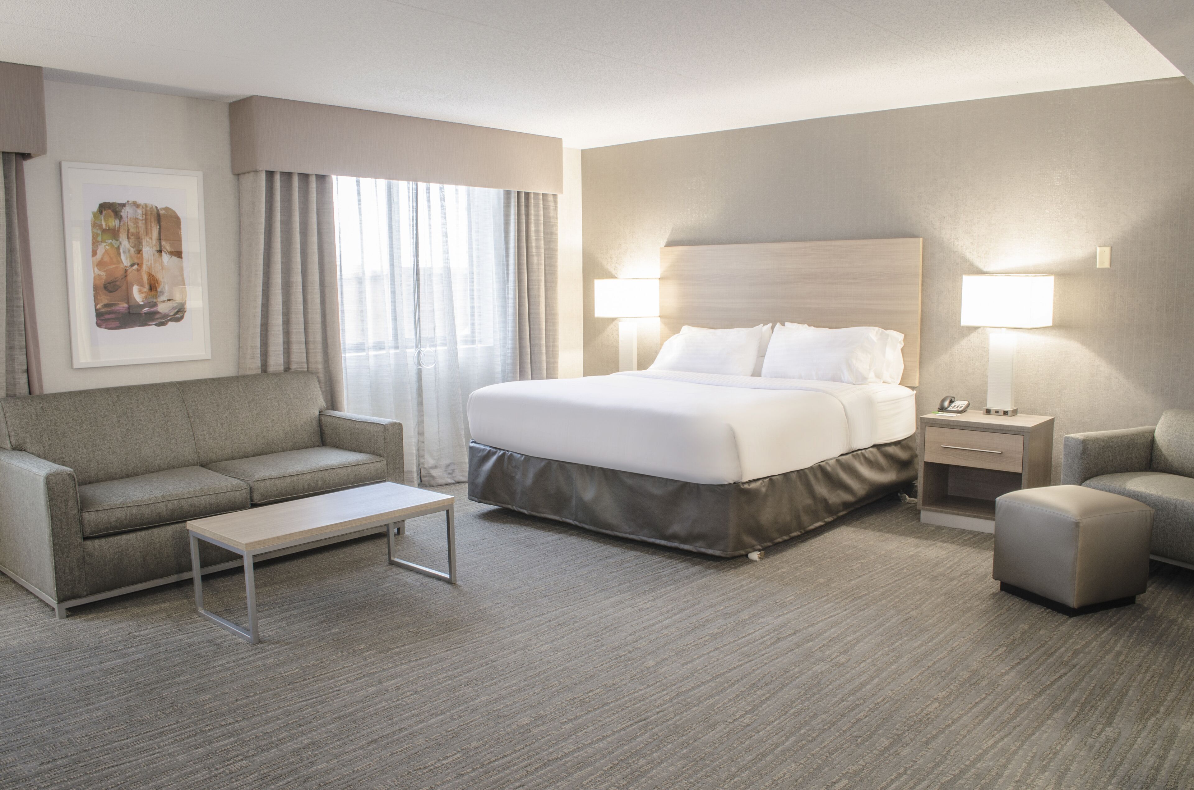 A hotel room with a bed, a sofa, a coffee table, two bedside tables with lamps, and a framed picture on the wall.
