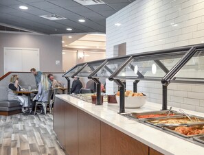 A buffet area with multiple food stations, a seating area with a sofa, and a counter with a bowl of bread. - Holiday Inn Fargo by IHG (Fargo)
