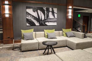 A modern hotel lobby with a sectional sofa, a small round table, and a large abstract painting on the wall.