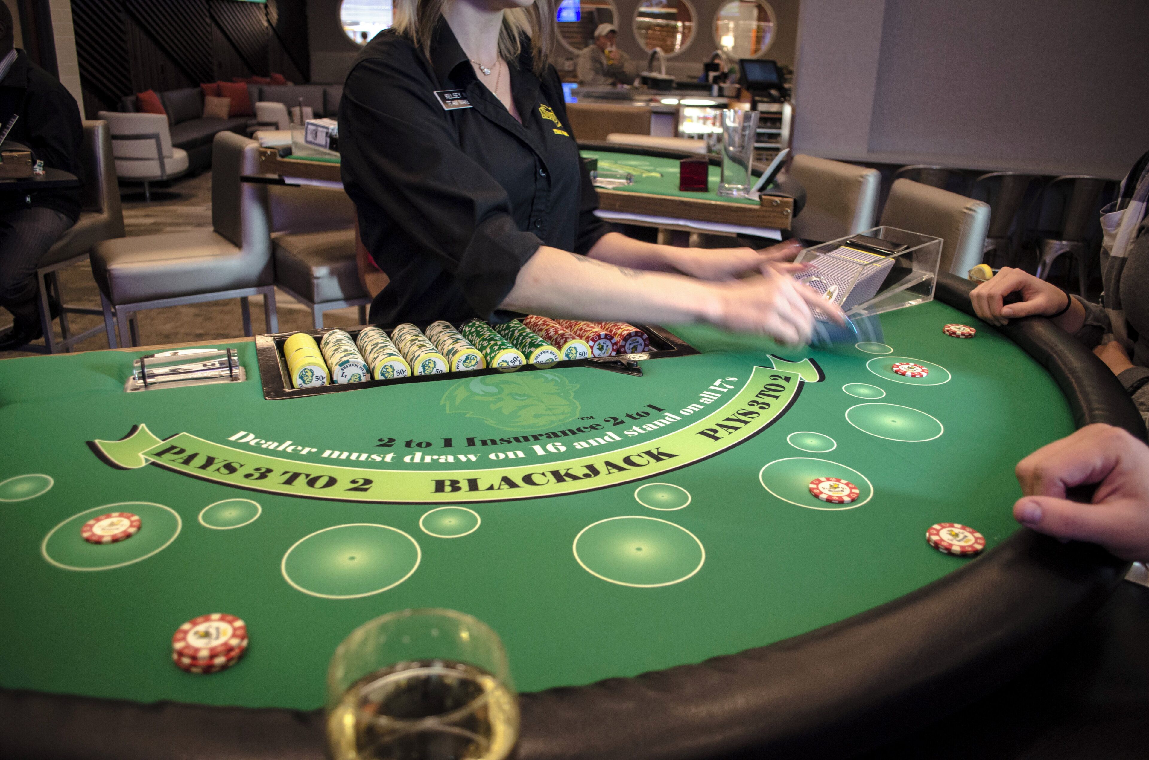 Une table de blackjack avec des jetons et des cartes, un croupier et un joueur.