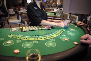Una mesa de blackjack con fichas, cartas, un crupier y un jugador.