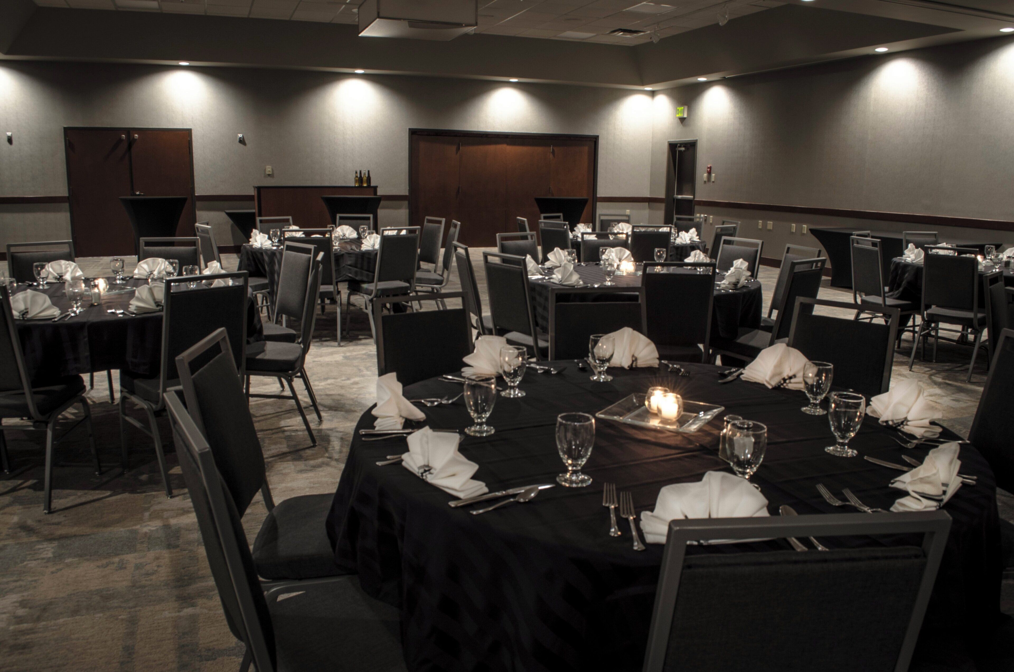 A conference room with multiple tables set for dining, equipped with chairs, tables, and candles.