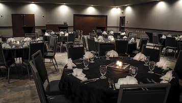 A conference room with multiple tables set for dining, equipped with chairs, tables, and candles.