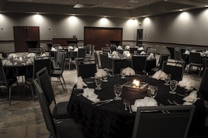 A conference room with multiple tables set for dining, equipped with chairs, tables, and candles.