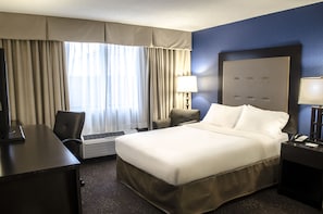 A hotel room with a large bed, a desk, a chair, a lamp, and a telephone.
