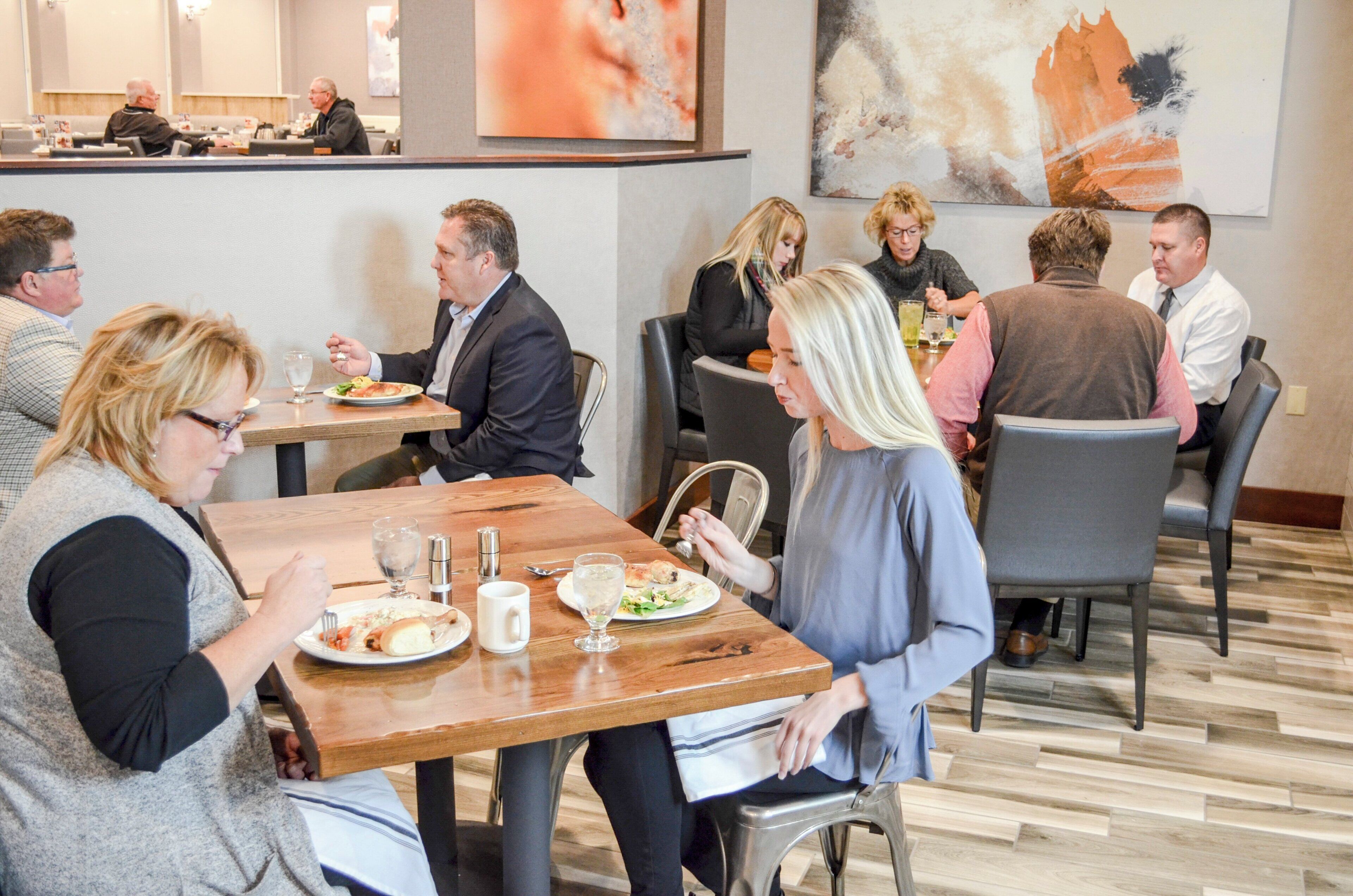 Un restaurant avec de nombreuses tables et chaises, des clients assis et différents plats servis dans des assiettes.