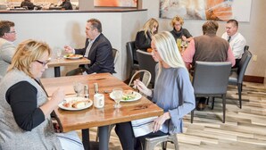 Un restaurant avec de nombreuses tables et chaises, des clients assis et différents plats servis dans des assiettes.
