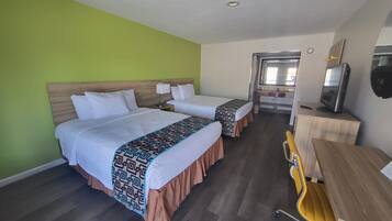 Une chambre d’hôtel avec deux lits, un bureau, une chaise, une télévision et une salle de bain visible au fond.
