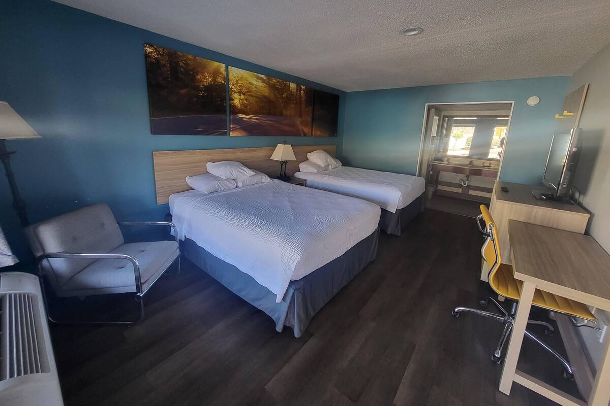 A hotel room with two beds, a desk, a chair, a TV, and a painting on the wall.