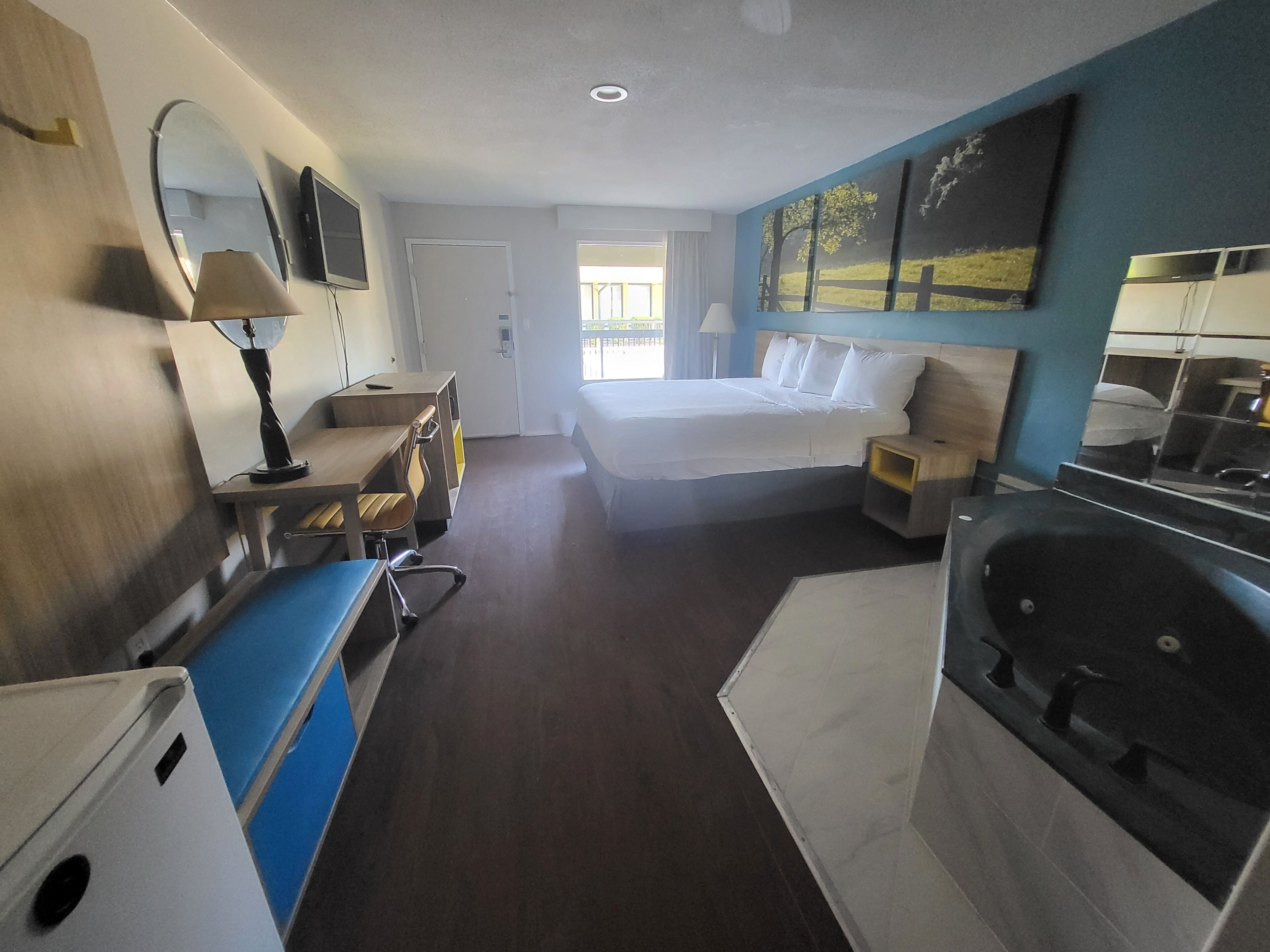 Habitación de hotel con cama, escritorio, silla, lámpara de escritorio, mesita de noche y bañera.