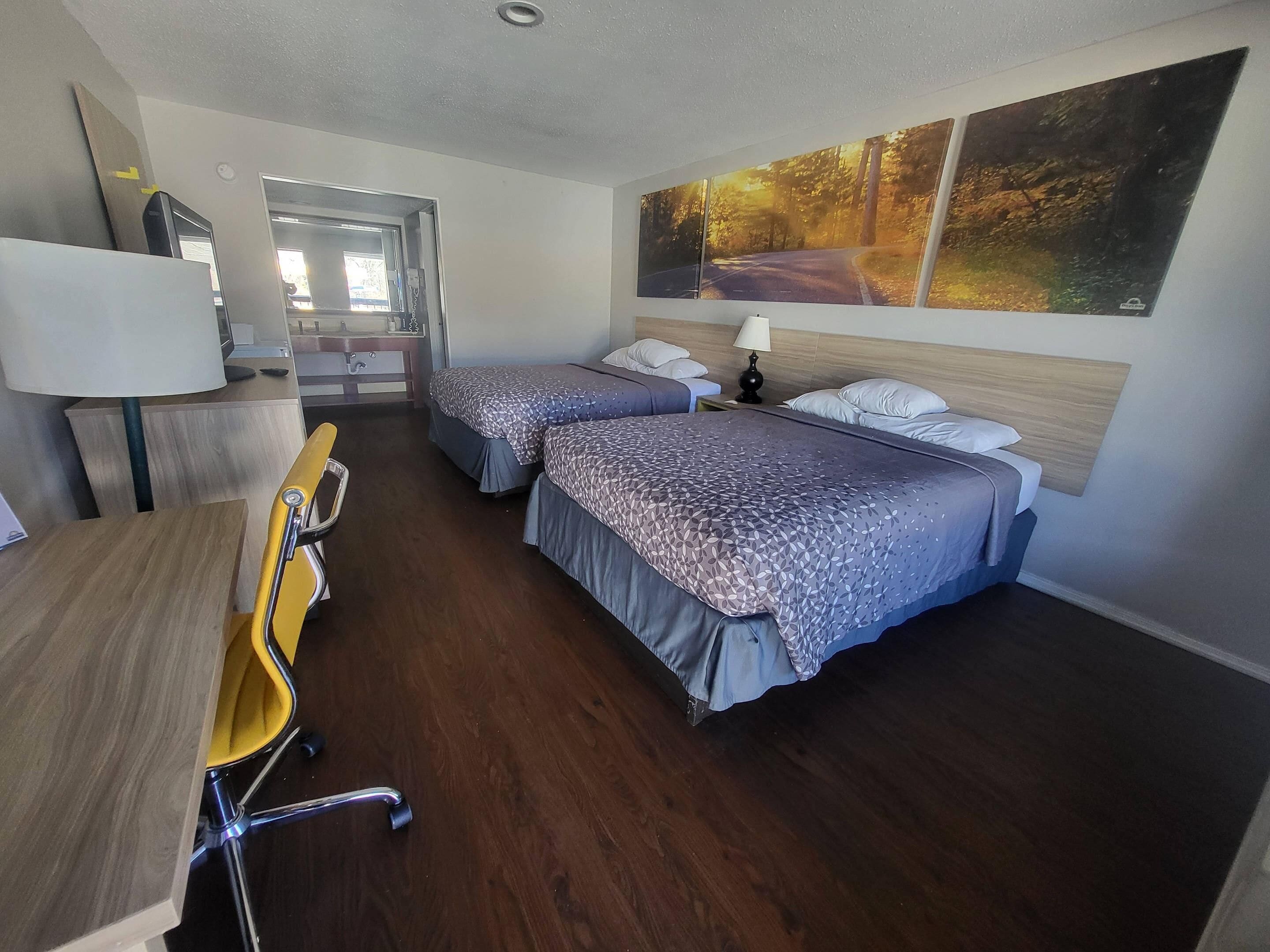 A hotel room with two beds, a desk, a chair, a lamp, and a painting on the wall.