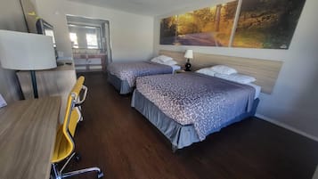 A hotel room with two beds, a desk, a chair, a lamp, and a painting on the wall.