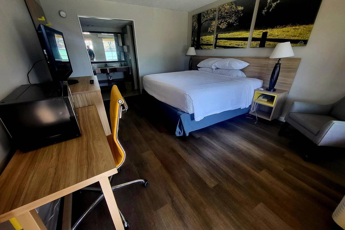 A hotel room with a bed, desk, chair, and a TV.