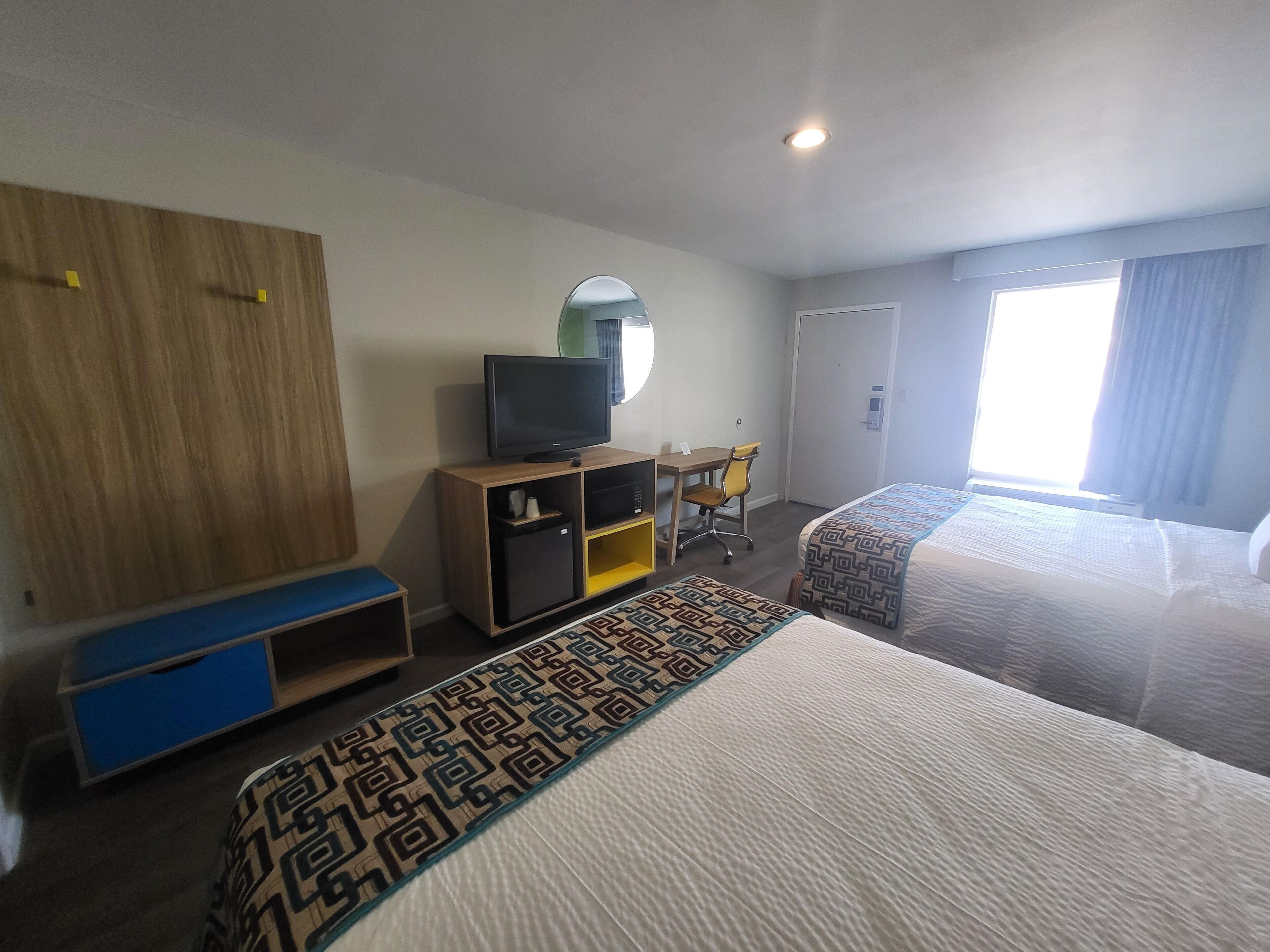 A hotel room with two beds, a desk with a chair, a television on a wooden cabinet, and a mirror on the wall.