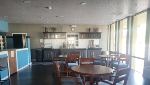 A modern kitchen with dark wood cabinets, a central island, and a dining area with wooden tables and chairs. - Park Inn by Radisson, Attalla-Gadsden (Attalla)