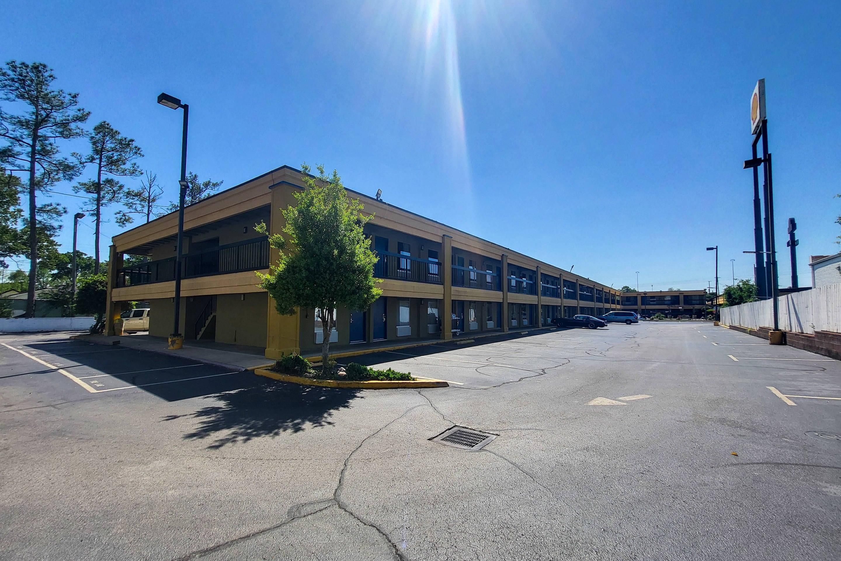 A multi-story building with a parking lot, a tree, and a clear sky.