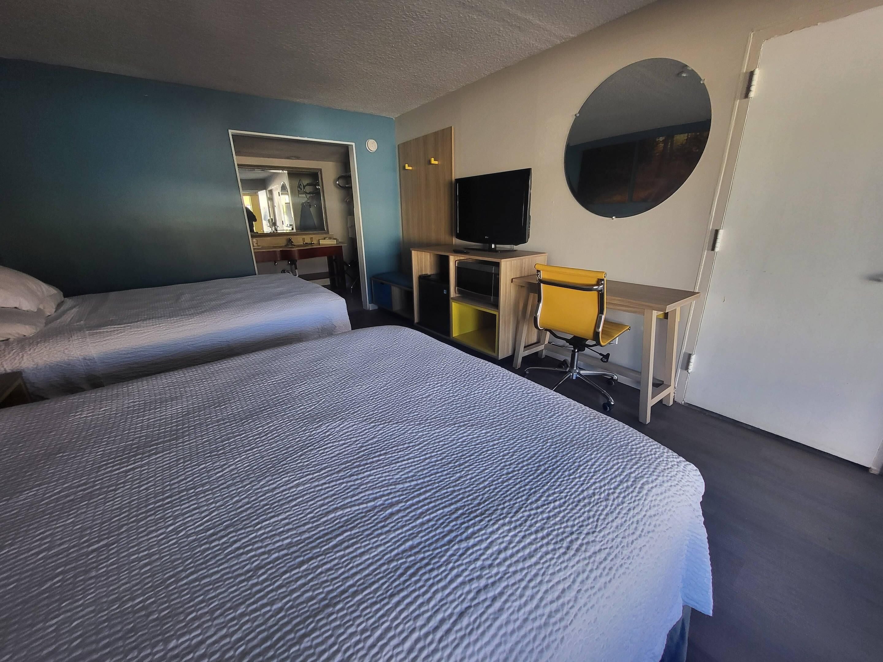 A hotel room with two beds, a desk, a chair, a television, and a mirror.