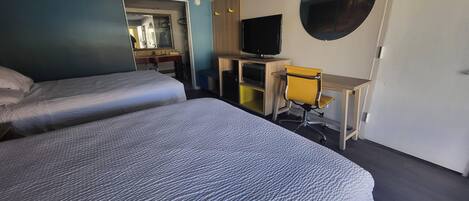 A hotel room with two beds, a desk, a chair, a television, and a mirror.