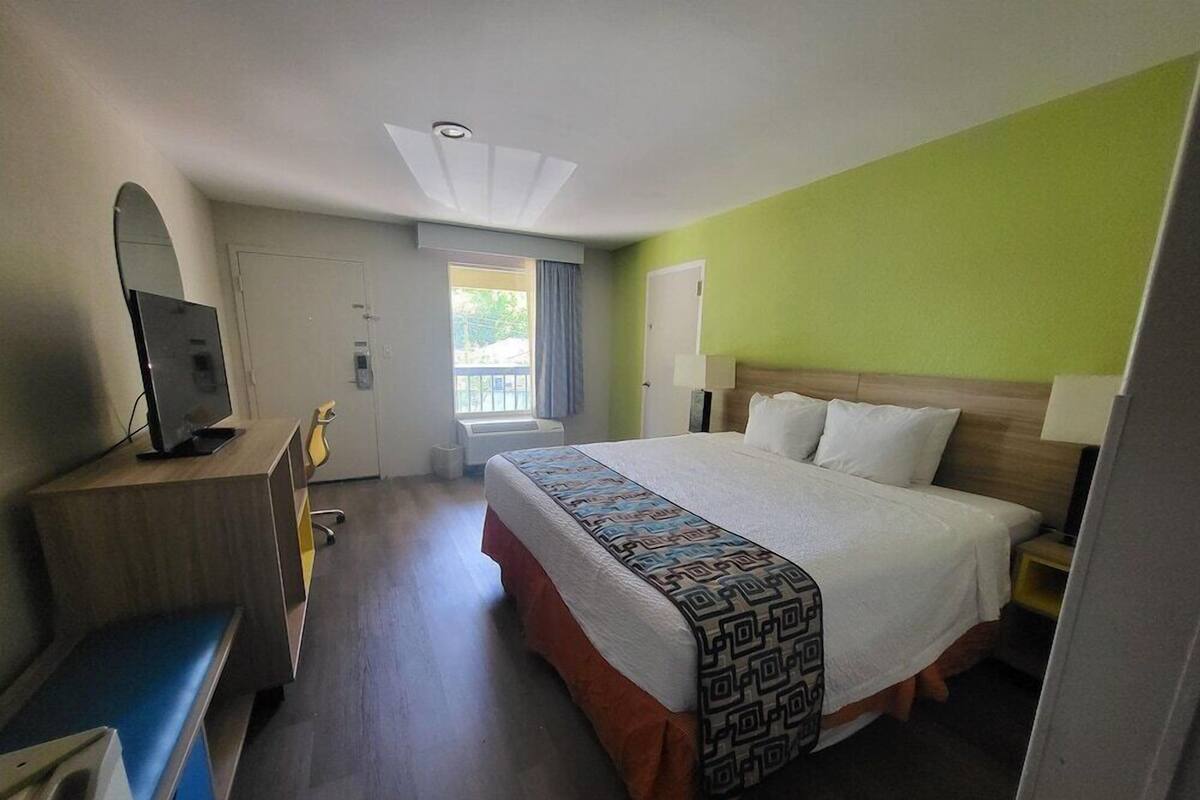 A hotel room with a bed, a desk with a computer, a TV, and a window.