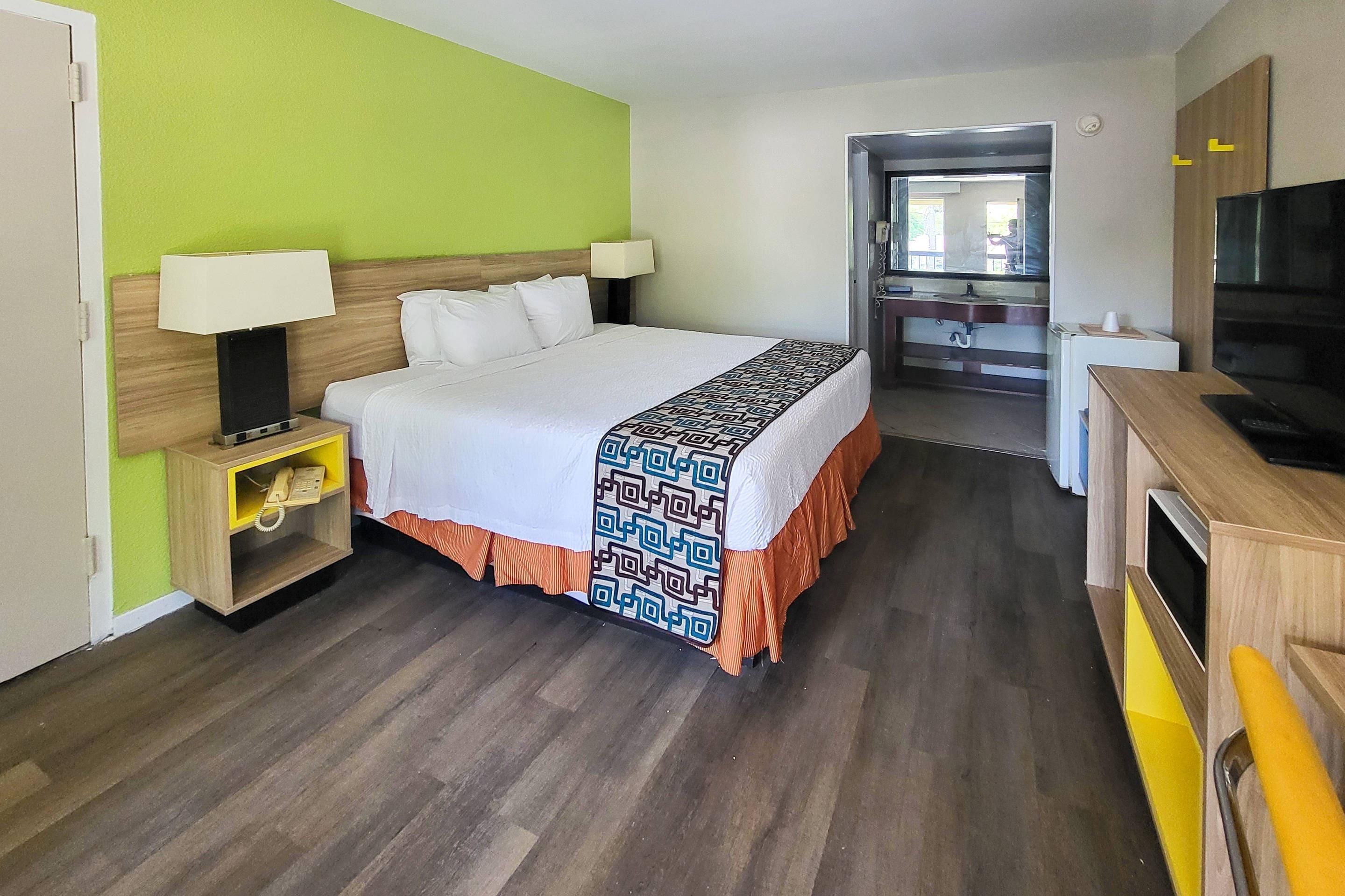 A hotel room with a bed, bedside lamps, a telephone, a TV, and a kitchenette area.