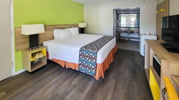 A hotel room with a bed, bedside lamps, a telephone, a TV, and a kitchenette area.