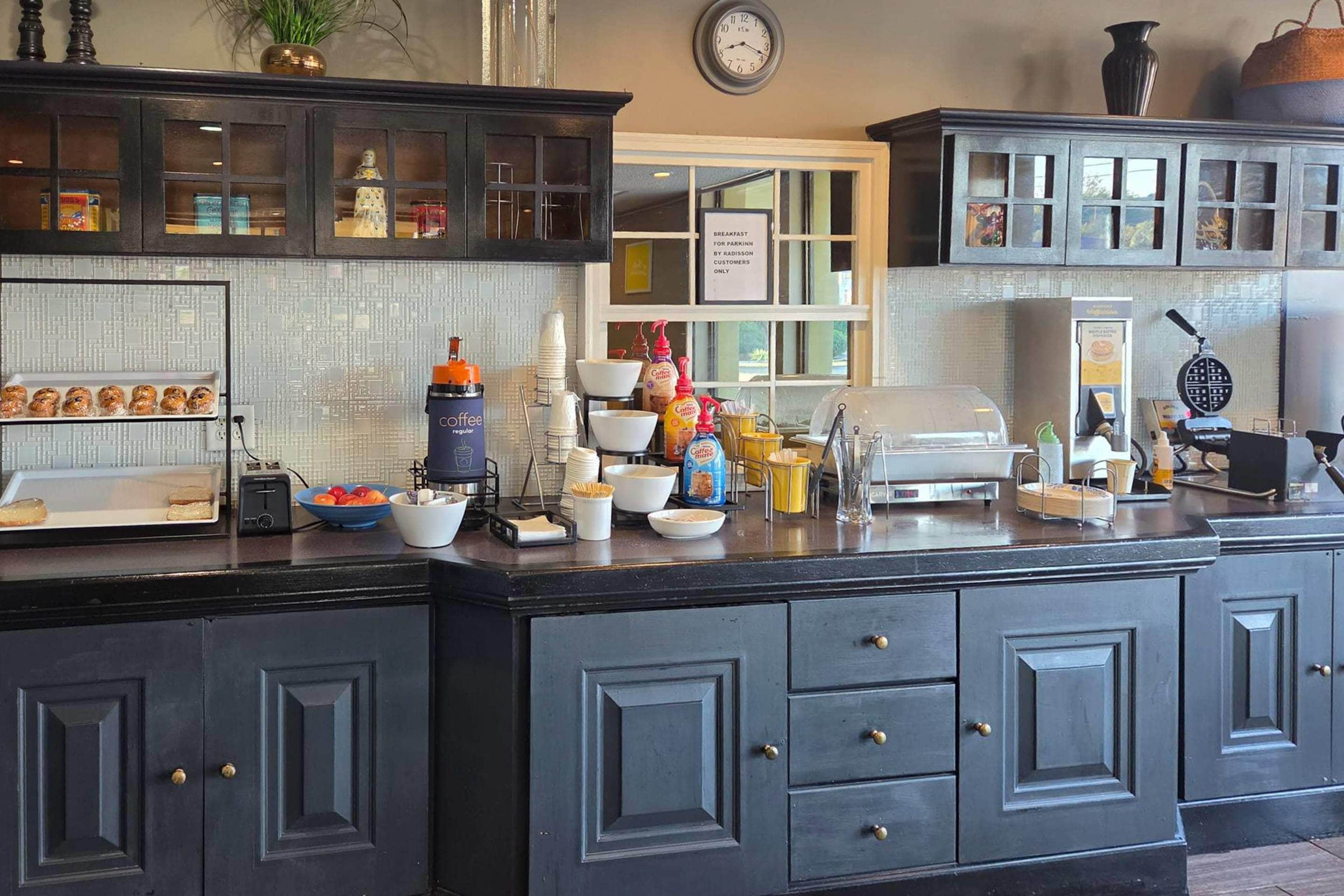 A breakfast bar with coffee and pastries, a clock, and a sign indicating breakfast for parkinn by radisson customers only.