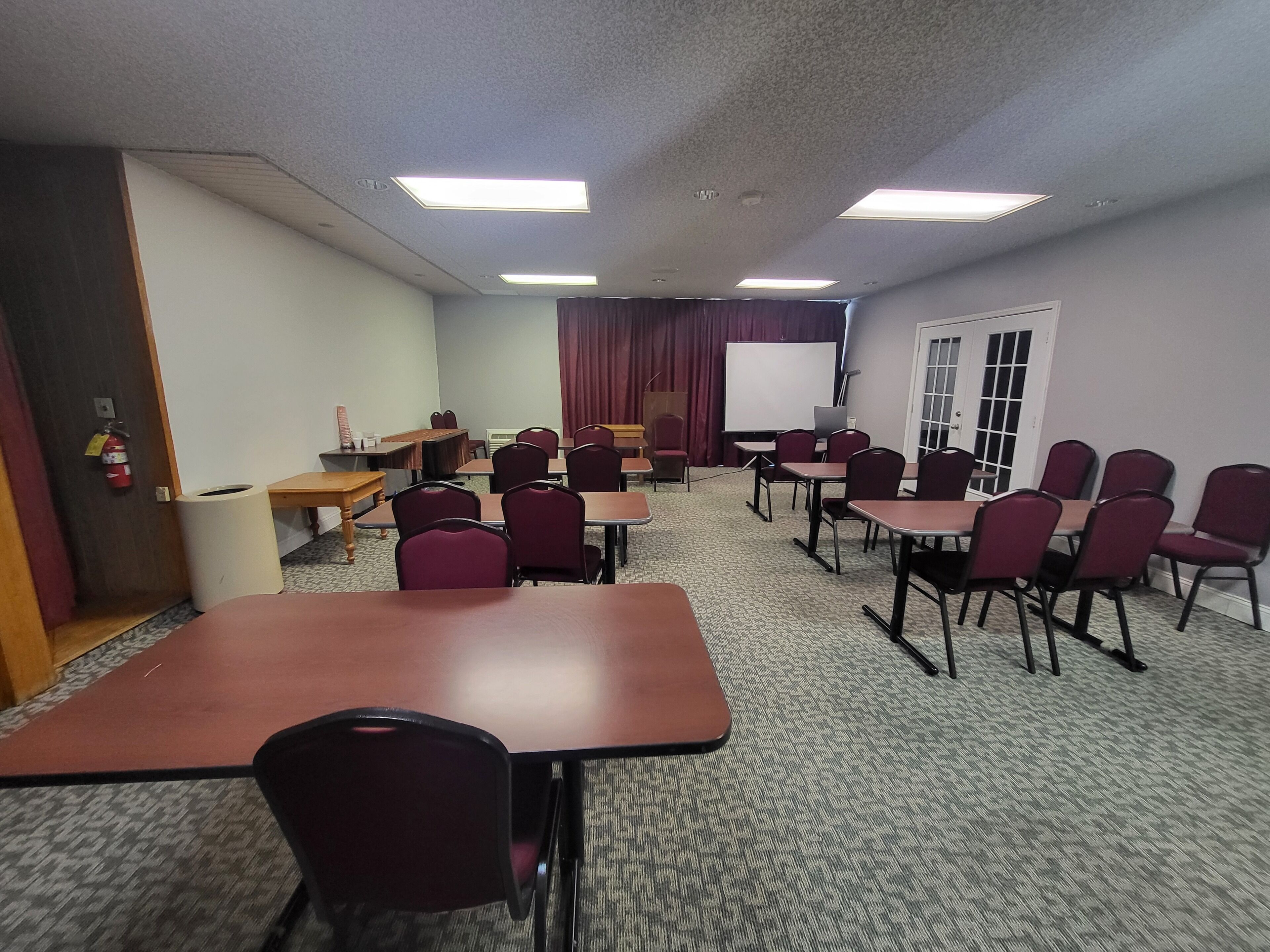 A conference room with tables, chairs, a whiteboard, and a projector screen.