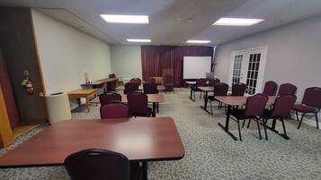A conference room with tables, chairs, a whiteboard, and a projector screen.