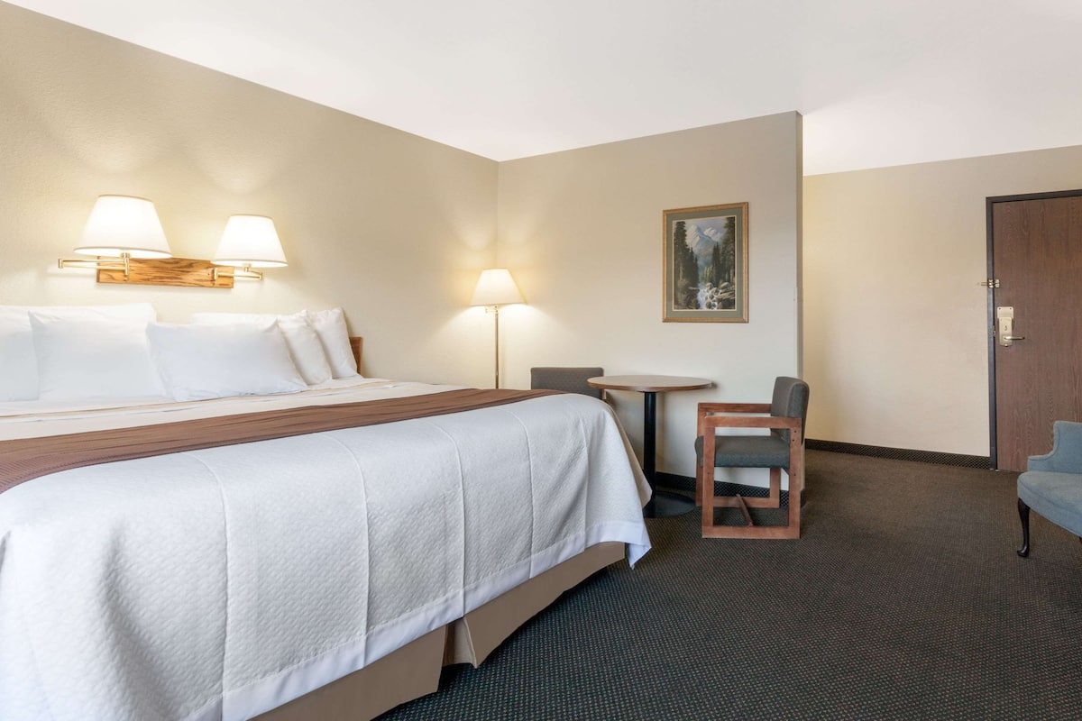 Een hotelkamer met een groot bed, twee bedlampen, een kleine tafel, een stoel en een deur.