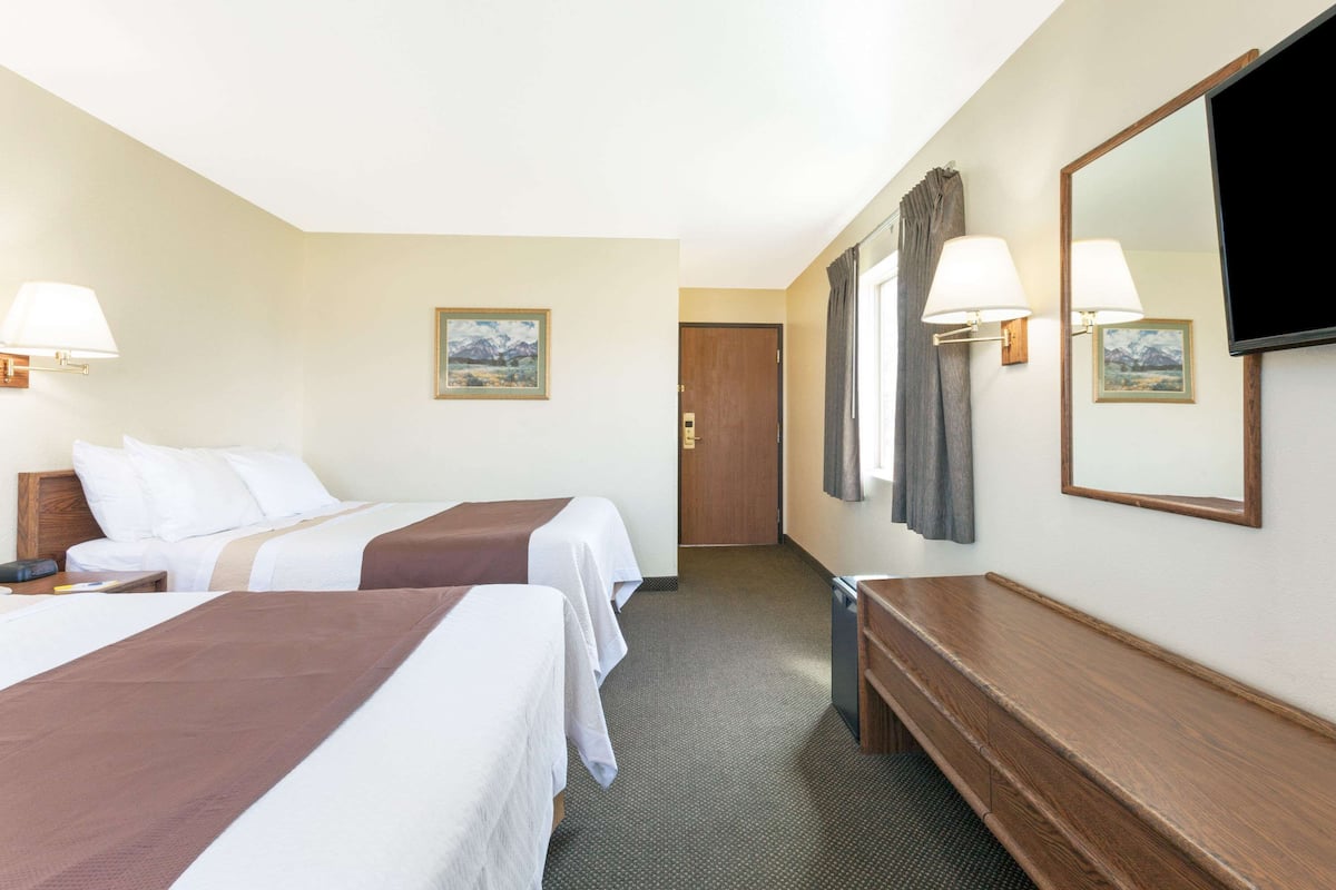 Een hotelkamer met twee bedden, een houten bankje, een televisie en een deur naar een andere kamer.
