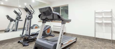 Un gimnasio con cintas de correr, elípticas y un espejo grande.