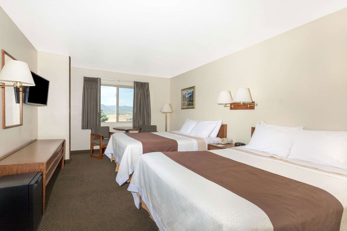 Een hotelkamer met twee bedden, een bureau, een stoel, een televisie, een raam met gordijnen en een schilderij aan de muur.