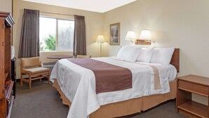 Una habitación de hotel con una cama grande, una silla, un escritorio y una ventana con cortinas.