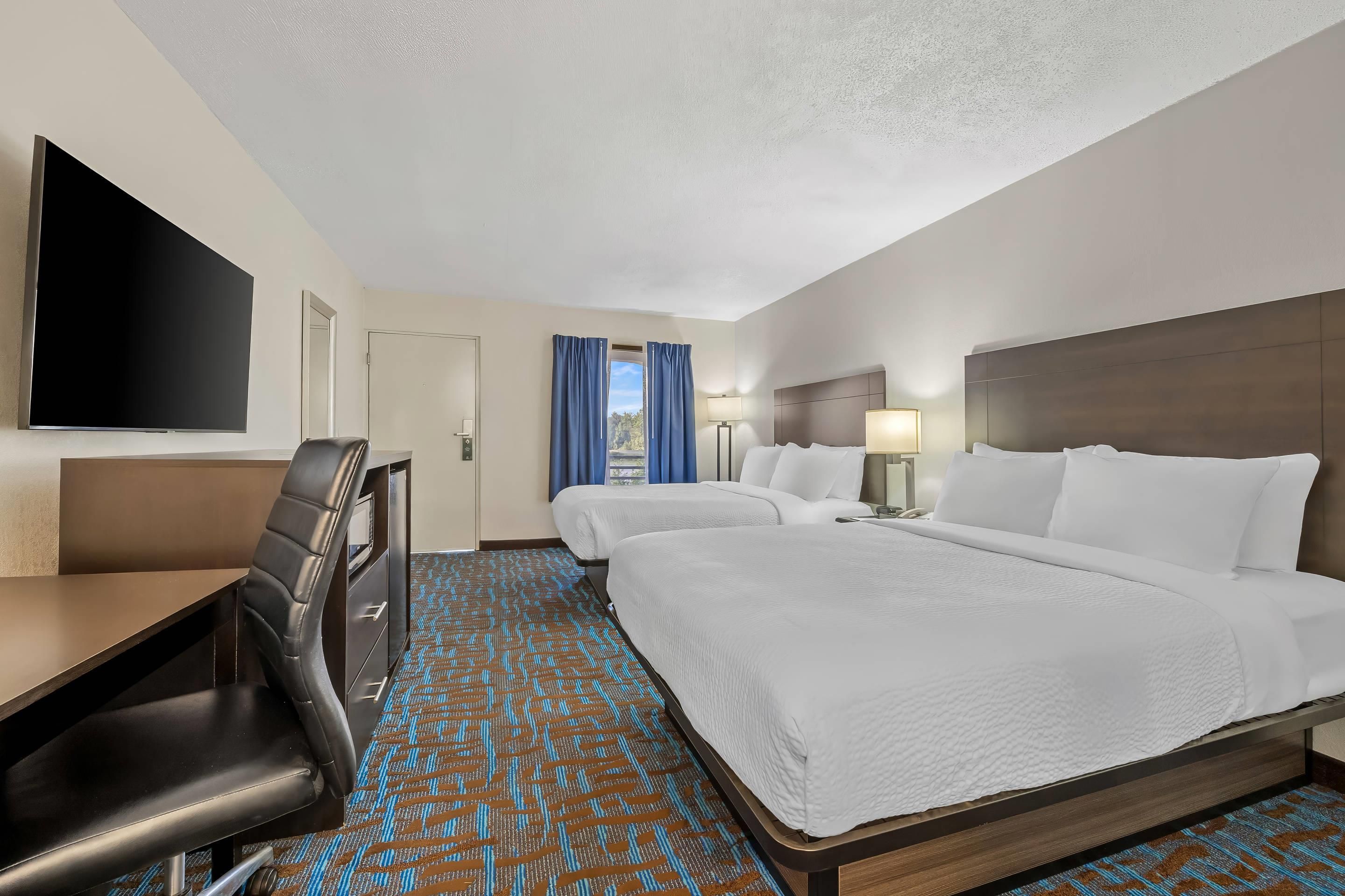 A hotel room with two beds, a desk, a chair, a TV, and a window with curtains.