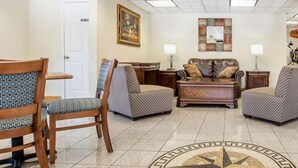 A lobby with a patterned rug, wooden chairs, a sofa, and a painting on the wall.