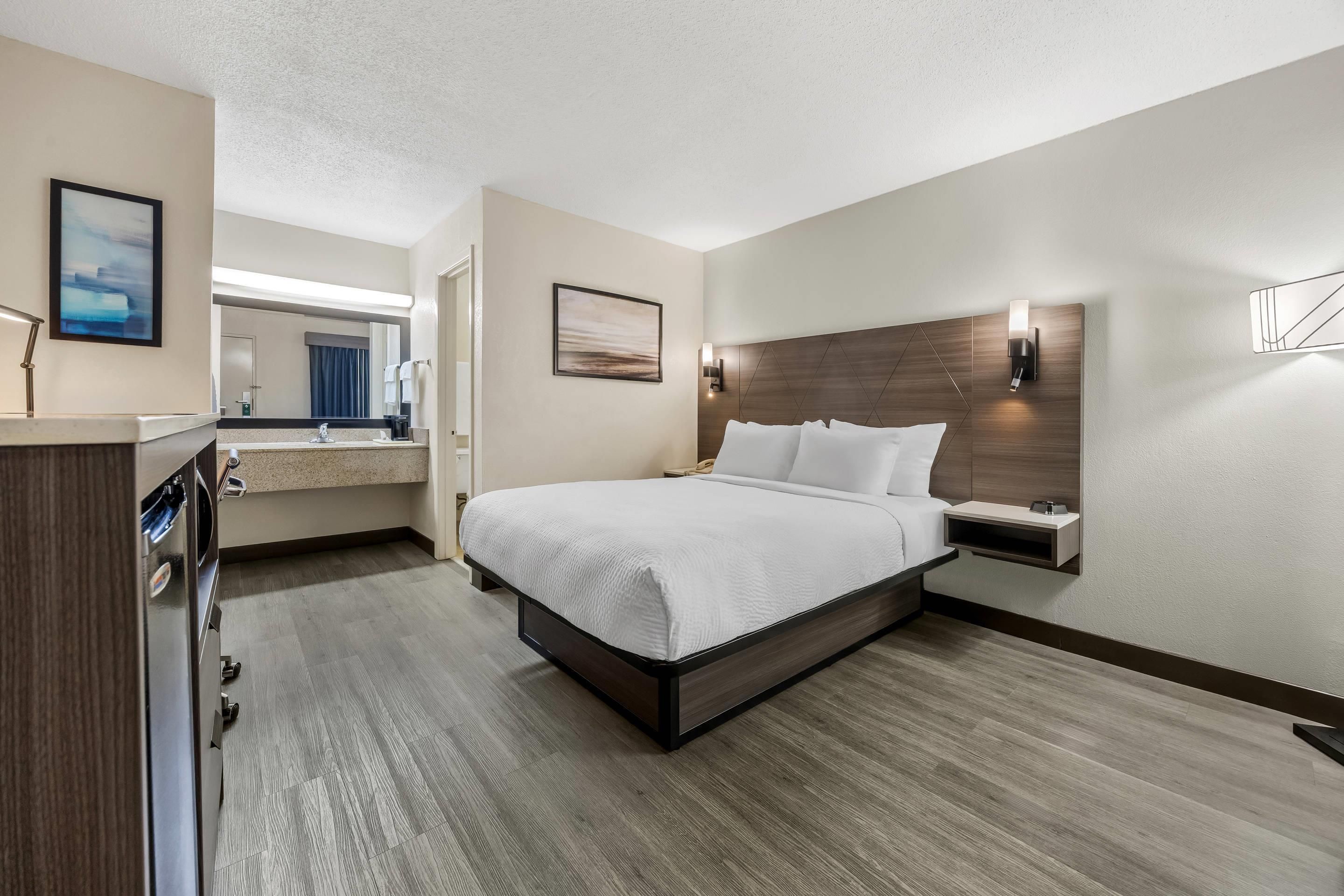 Habitación de hotel con cama, mesita de noche, espejo y lámpara de pared.
