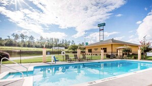 A pool area with a sign for Quality Inn, a fenced patio with chairs, and a clear sky.