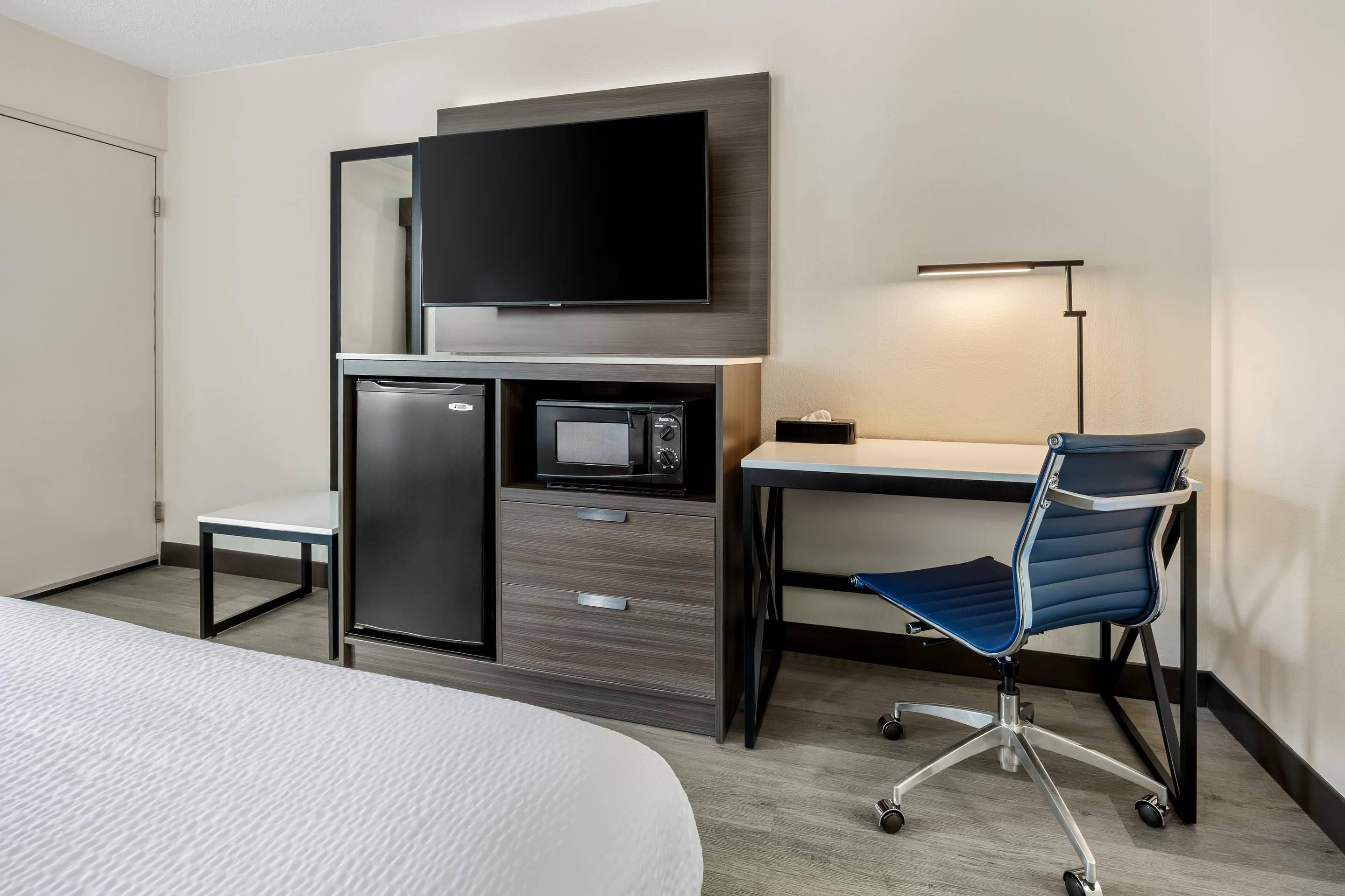 Une chambre d’hôtel équipée d’un lit, d’un bureau, d’une chaise, d’une télévision, d’un four à micro-ondes et d’un petit réfrigérateur.
