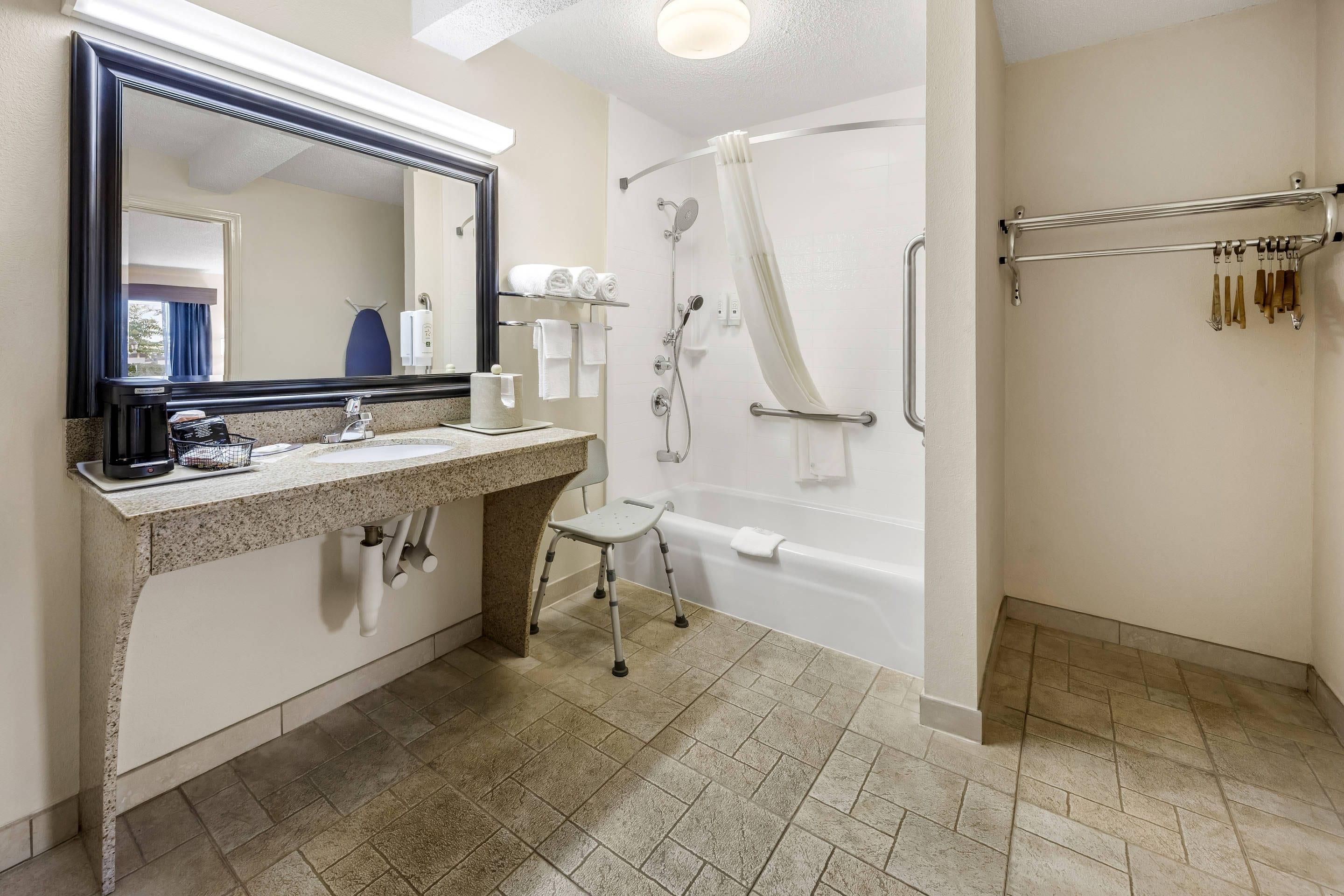 A bathroom with a sink, mirror, towel rack, shower, and a grab bar.
